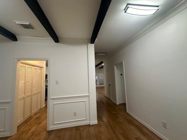 hallway featuring visible vents, ornamental molding, wood finished floors, beamed ceiling, and baseboards