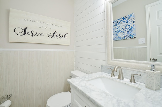 half bath featuring toilet, wooden walls, vanity, and wainscoting