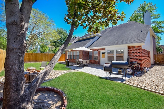 back of property featuring a patio, a fenced backyard, brick siding, a yard, and a chimney