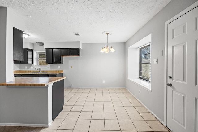 kitchen featuring light tile patterned floors, a chandelier, a peninsula, visible vents, and dark cabinetry