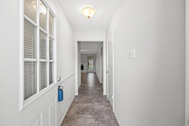 hall featuring a textured ceiling and baseboards