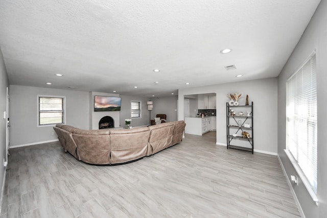 living area with light wood-type flooring, a fireplace, baseboards, and recessed lighting