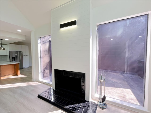 interior space with recessed lighting, lofted ceiling, a fireplace with raised hearth, and light wood finished floors