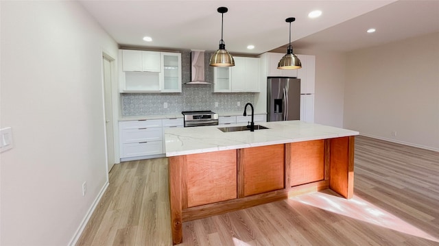 kitchen featuring a sink, decorative backsplash, stainless steel appliances, light wood-style floors, and wall chimney exhaust hood