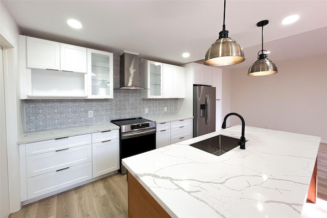 kitchen featuring a sink, backsplash, stainless steel appliances, light wood-style floors, and wall chimney exhaust hood