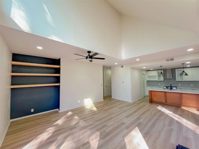 unfurnished living room with visible vents, high vaulted ceiling, a sink, ceiling fan, and light wood-type flooring