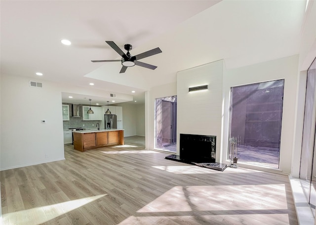 unfurnished living room featuring a ceiling fan, visible vents, light wood-style flooring, a fireplace with raised hearth, and a sink