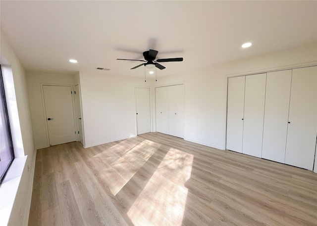 unfurnished bedroom with light wood-type flooring, visible vents, two closets, recessed lighting, and ceiling fan