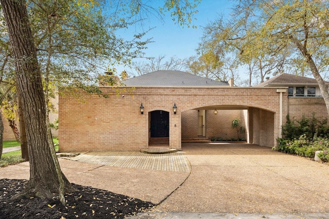 view of front facade featuring brick siding, a chimney, and driveway