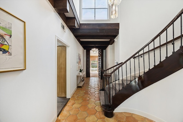 entrance foyer with visible vents, baseboards, a chandelier, beamed ceiling, and stairway