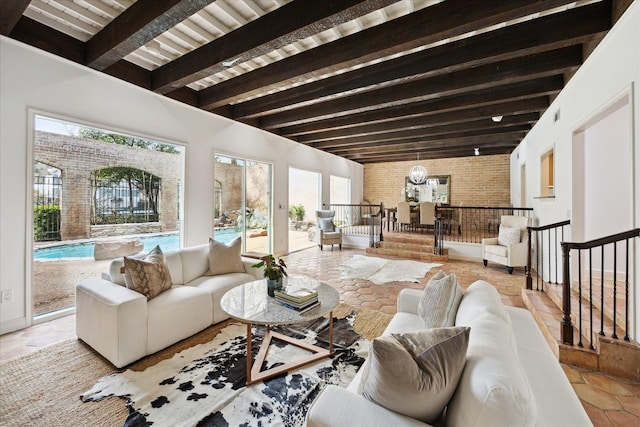 living area featuring a chandelier, beam ceiling, stone tile floors, and brick wall