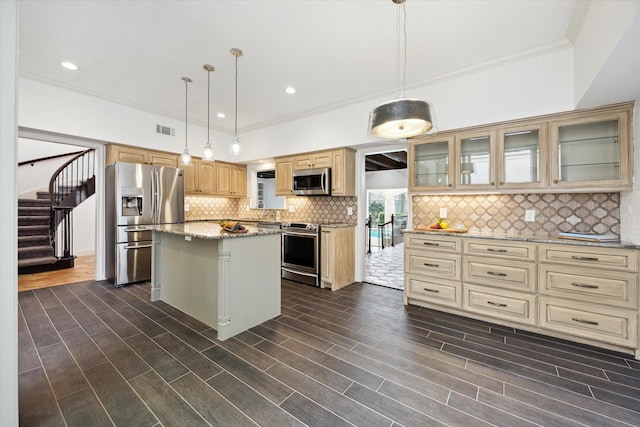 kitchen with appliances with stainless steel finishes, a center island, ornamental molding, light stone counters, and tasteful backsplash