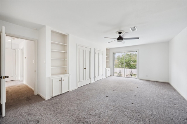 unfurnished living room with carpet flooring, a ceiling fan, and built in shelves