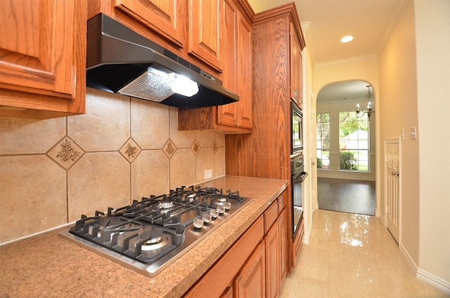 kitchen featuring arched walkways, stainless steel gas cooktop, decorative backsplash, oven, and under cabinet range hood