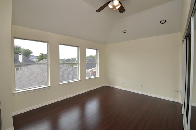 spare room featuring dark wood-style floors, lofted ceiling, a ceiling fan, and baseboards