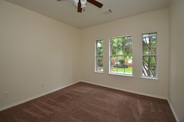 spare room with dark colored carpet, visible vents, ceiling fan, and baseboards