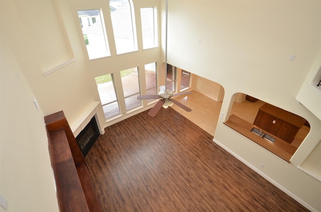 unfurnished living room featuring a towering ceiling, a fireplace, baseboards, and dark wood-style flooring