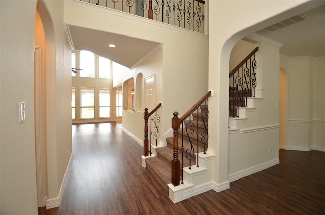 stairway featuring baseboards, arched walkways, wood finished floors, a high ceiling, and crown molding