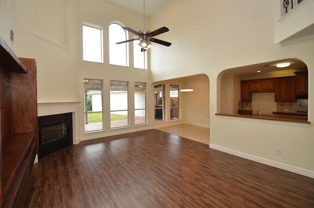 unfurnished living room featuring baseboards, arched walkways, a ceiling fan, a glass covered fireplace, and wood finished floors