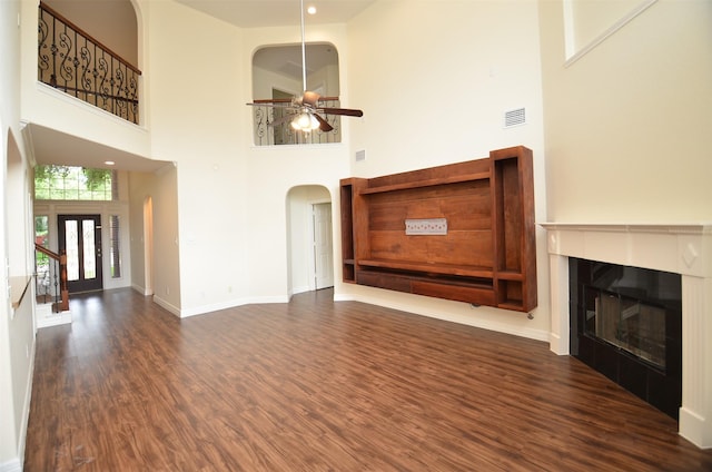 unfurnished living room with visible vents, arched walkways, a glass covered fireplace, ceiling fan, and wood finished floors