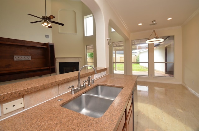 kitchen with light stone counters, crown molding, a fireplace, pendant lighting, and a sink