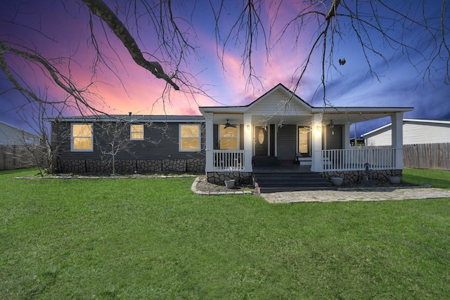 view of front of home featuring a porch, fence, and a lawn