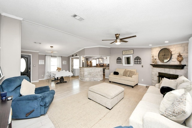 living room featuring visible vents, ornamental molding, a textured ceiling, a stone fireplace, and light wood-type flooring