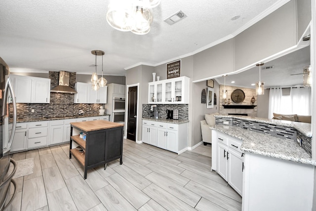 kitchen featuring wood counters, visible vents, wall chimney range hood, appliances with stainless steel finishes, and an inviting chandelier