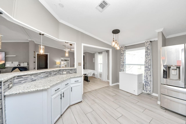 kitchen with wood finish floors, visible vents, vaulted ceiling, ornamental molding, and stainless steel fridge