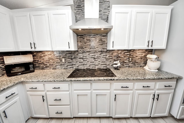 kitchen with black electric cooktop, white cabinetry, backsplash, light stone countertops, and wall chimney exhaust hood