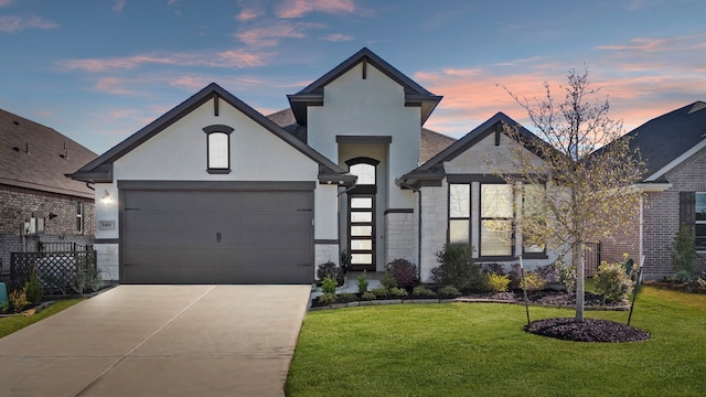 french country style house with stucco siding, a lawn, stone siding, concrete driveway, and an attached garage