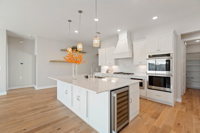 kitchen featuring a center island with sink, a sink, wine cooler, custom range hood, and appliances with stainless steel finishes