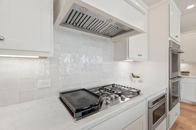 kitchen featuring stainless steel appliances, backsplash, exhaust hood, and white cabinetry