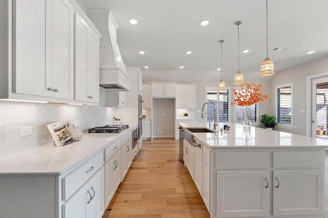 kitchen with premium range hood, double wall oven, light wood-style floors, stainless steel gas stovetop, and a sink