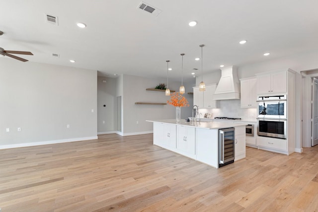 kitchen featuring visible vents, beverage cooler, premium range hood, and stainless steel double oven