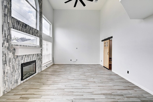 unfurnished living room featuring a fireplace, a high ceiling, a barn door, ceiling fan, and baseboards