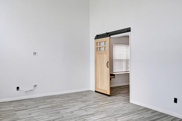 spare room with light wood-style flooring, baseboards, and a barn door