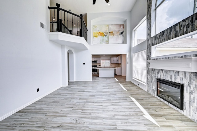 unfurnished living room with baseboards, visible vents, a glass covered fireplace, wood finished floors, and a high ceiling