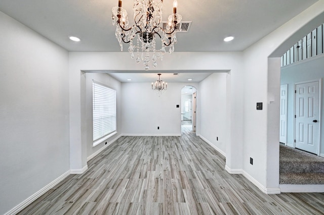 unfurnished dining area with arched walkways, a notable chandelier, wood finished floors, visible vents, and baseboards