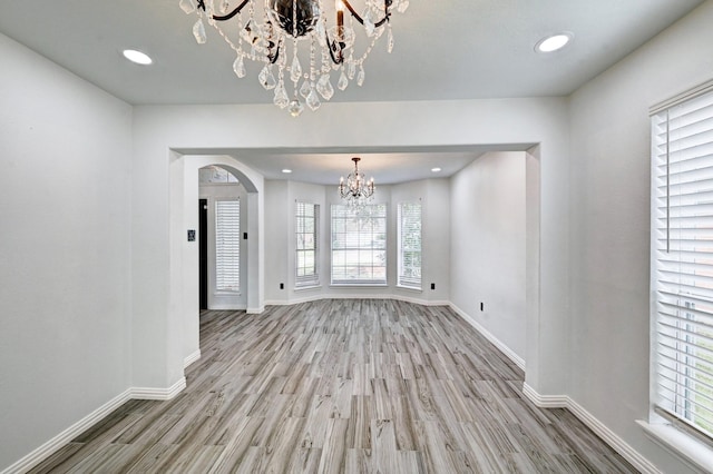 unfurnished dining area with arched walkways, wood finished floors, baseboards, and an inviting chandelier