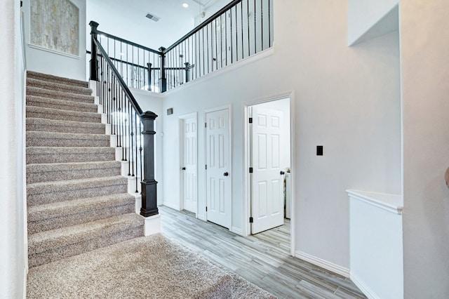 stairway with visible vents, a towering ceiling, baseboards, and wood finished floors