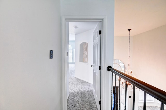 corridor with carpet, a chandelier, and baseboards