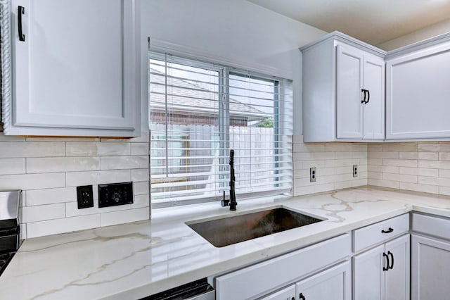 kitchen featuring light stone counters, backsplash, a sink, and white cabinetry