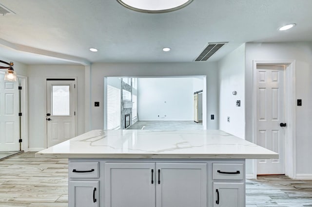 kitchen featuring light stone countertops, light wood finished floors, a fireplace, and visible vents