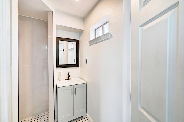 bathroom with baseboards, a tile shower, and vanity