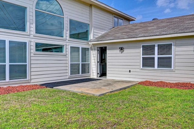 property entrance with a patio, a yard, and a shingled roof