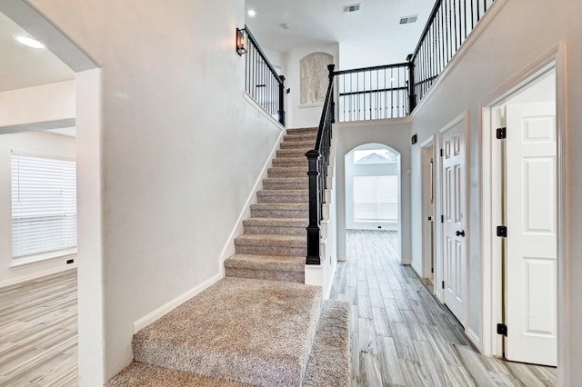 staircase with arched walkways, wood finished floors, visible vents, and baseboards