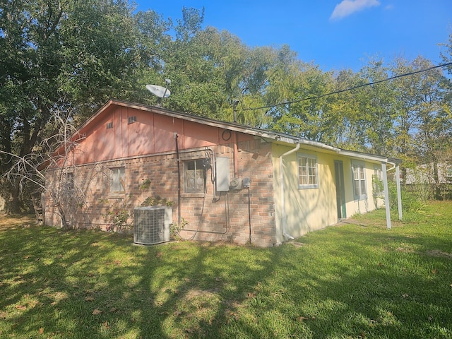 view of side of home with brick siding, a lawn, and cooling unit