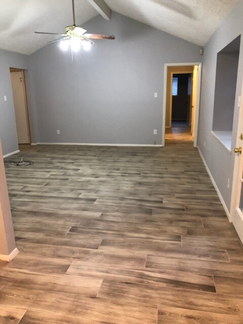 spare room featuring baseboards, vaulted ceiling with beams, ceiling fan, and wood finished floors