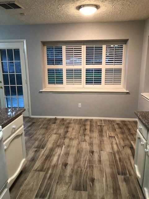 unfurnished dining area featuring dark wood-style floors, visible vents, a textured ceiling, and baseboards